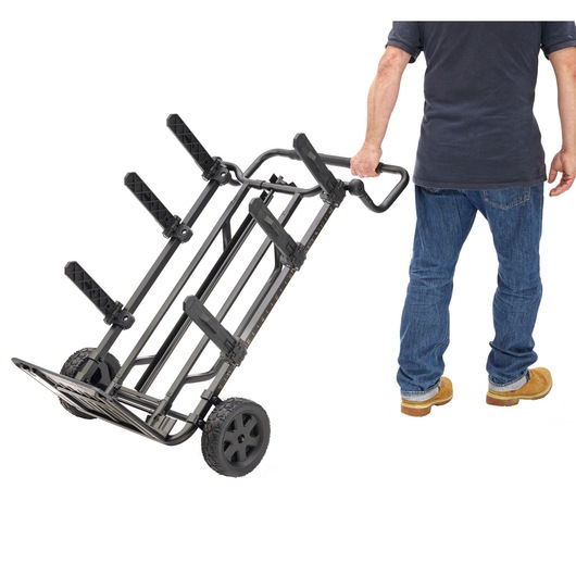 A person is pulling a DEWALT foldable hand truck with large wheels and adjustable support arms, designed for transporting heavy or bulky items.