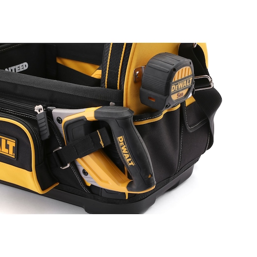 Close-up of a DEWALT tool bag featuring a DEWALT staple gun and a DEWALT 5-meter measuring tape attached to its side. The bag is made of black and yellow durable material and has multiple compartments and pockets.