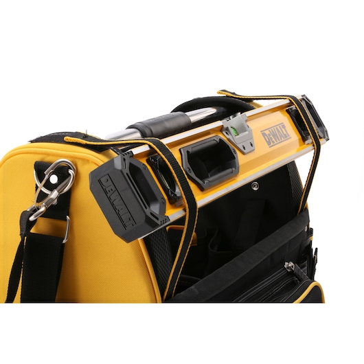 Close-up of a yellow and black DEWALT tool bag with a level secured on top using a strap. The tool bag has a shoulder strap with a metal clip.