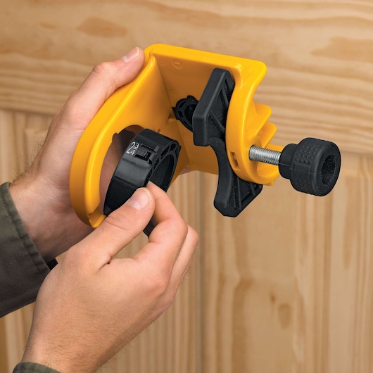 A close-up of hands adjusting a yellow and black DEWALT door lock installation tool against a wooden door. The tool is designed to help with accurate placement for drilling holes for handles and locks.
