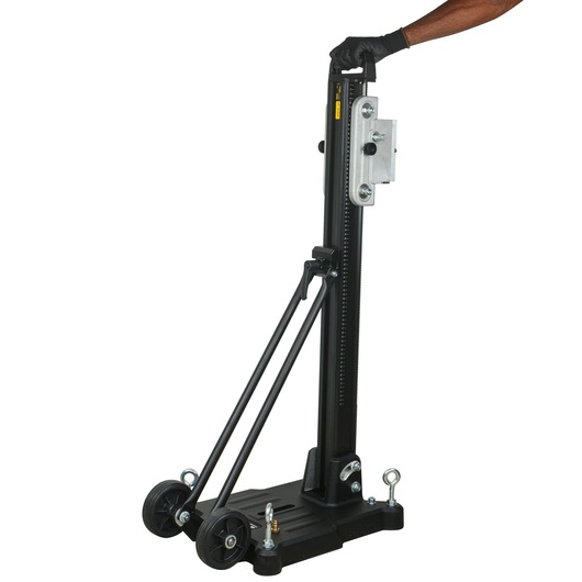 A DEWALT portable drill stand with wheels, featuring a vertical column, metal attachments, and a base. A person wearing a black glove is holding the handle at the top of the stand.