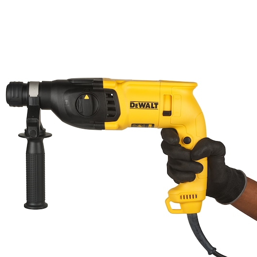 A person wearing a black glove is holding a yellow and black DEWALT electric hammer drill with a side handle.