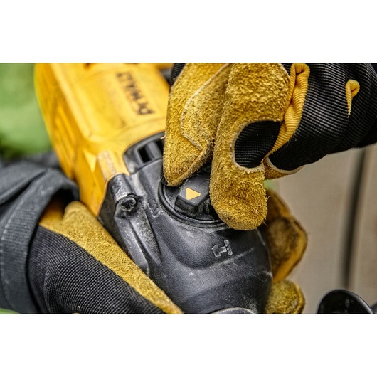 Close-up of a person wearing yellow and black work gloves adjusting a mode selector switch on a DEWALT power tool.