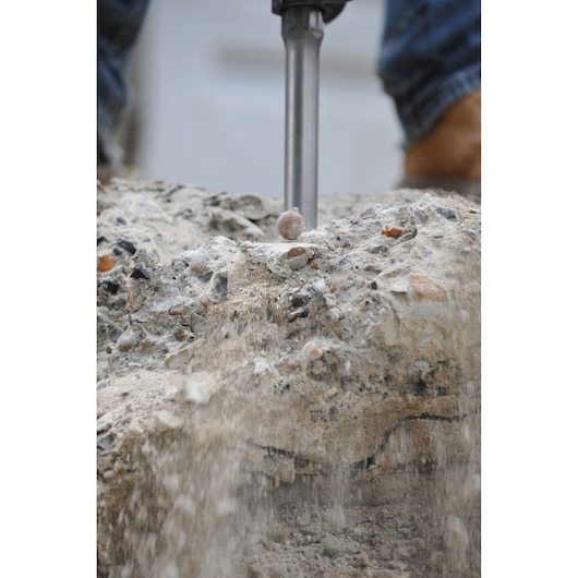 Close-up of a demolition hammer breaking concrete, with dust and debris falling as the tool is used.