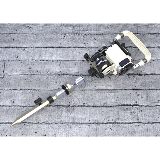 A mechanical tool with a pointed metal tip, various gears, and a handle, placed on a textured concrete surface.