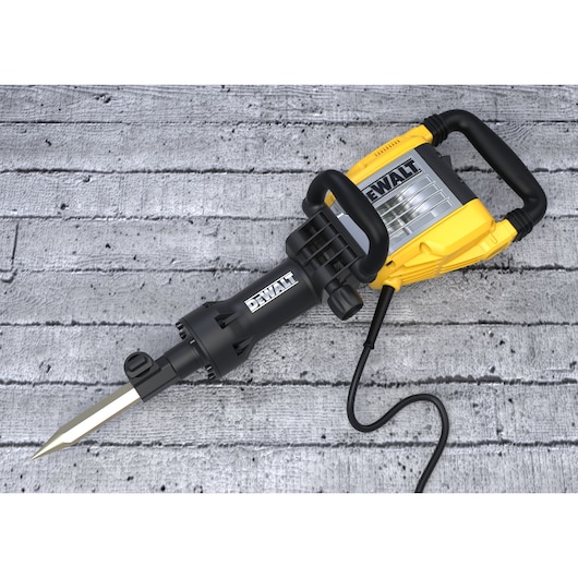 A yellow and black DEWALT demolition hammer with a pointed chisel attachment, placed on a gray concrete surface.