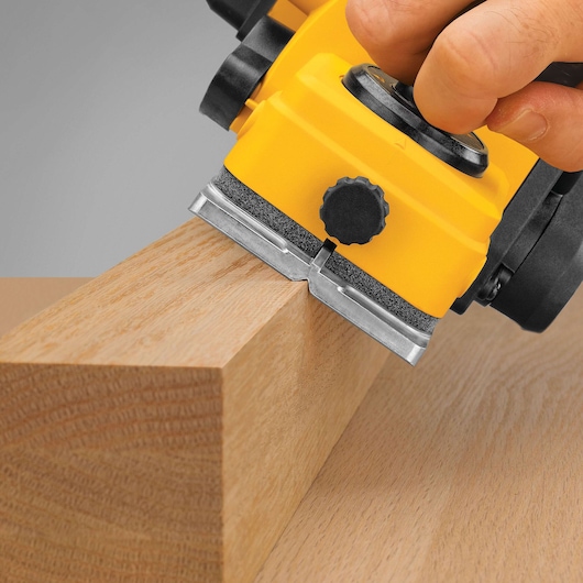 Close-up of a yellow DEWALT electric planer being used to smooth the edge of a wooden plank.