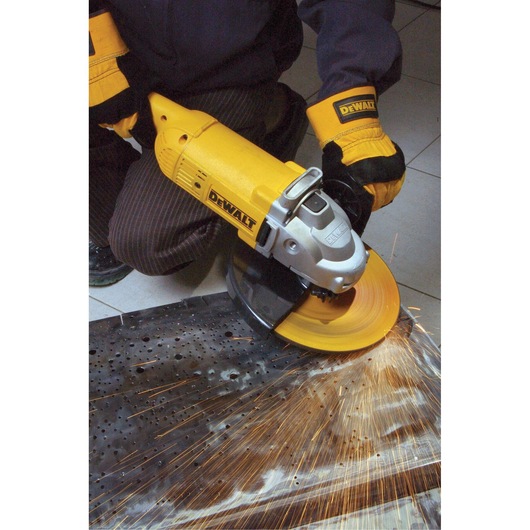 A person wearing protective gloves is using a yellow DEWALT angle grinder to cut or grind a metal surface, with sparks flying from the contact point.