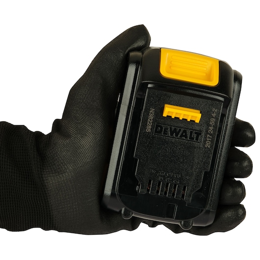 A black gloved hand holding a DEWALT DCB181 battery pack, showing the connectors and yellow release button.