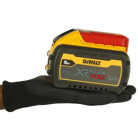 A DeWalt XR FlexVolt 18V/54V 9Ah lithium-ion battery is shown resting on a gloved hand. The battery has yellow, black, and red detailing and is labeled with its specifications.