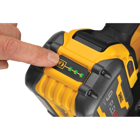 A close-up of a hand pressing the battery indicator button on a yellow and black DEWALT 9Ah FLEXVOLT battery, showing three green lights.