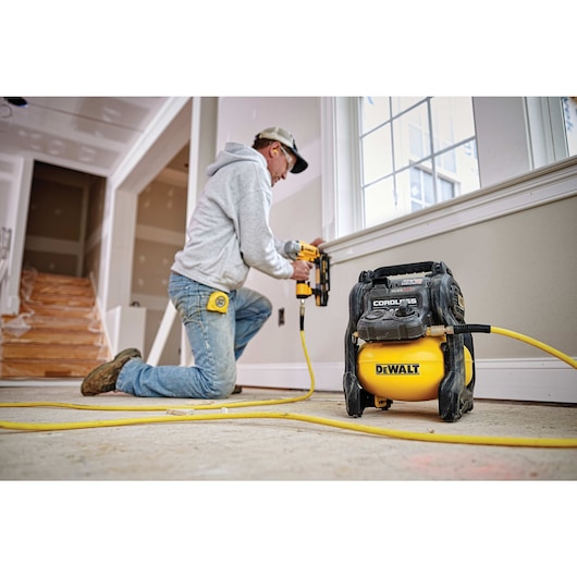 FLEXVOLT® 2.5 GALLON CORDLESS AIR COMPRESSOR being used by a person to power a pneumatic nailer for countersinking holes in a wooden window frame