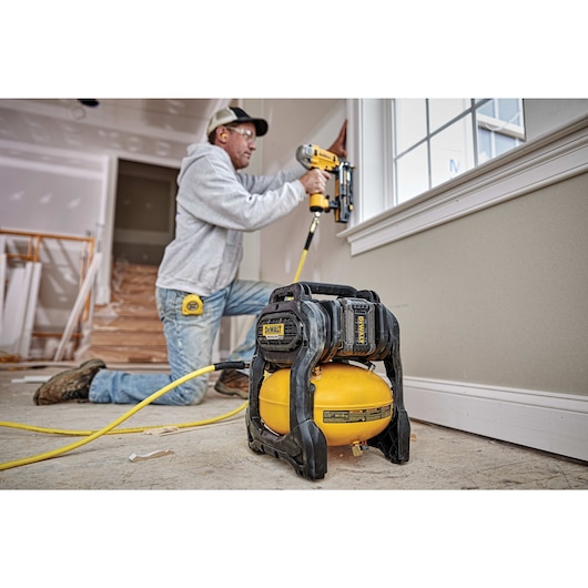 FLEXVOLT® 2.5 GALLON CORDLESS AIR COMPRESSOR being used by a person to power a pneumatic nailer for countersinking holes in a wooden window frame