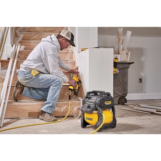 FLEXVOLT® 2.5 GALLON CORDLESS AIR COMPRESSOR being used by a person to power a pneumatic nailer for countersinking holes in a wooden frame around stairs