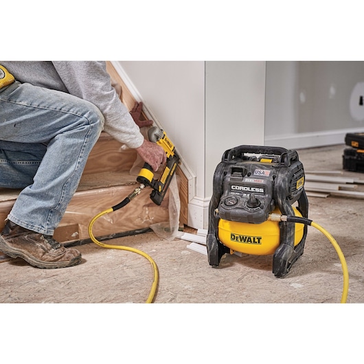 FLEXVOLT® 2.5 GALLON CORDLESS AIR COMPRESSOR being used by a person to power a pneumatic nailer for countersinking holes in wooden frame around stairs