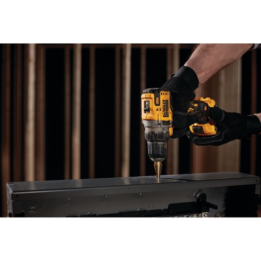 A person wearing black gloves using a yellow DEWALT cordless drill to make a hole in a metal surface.