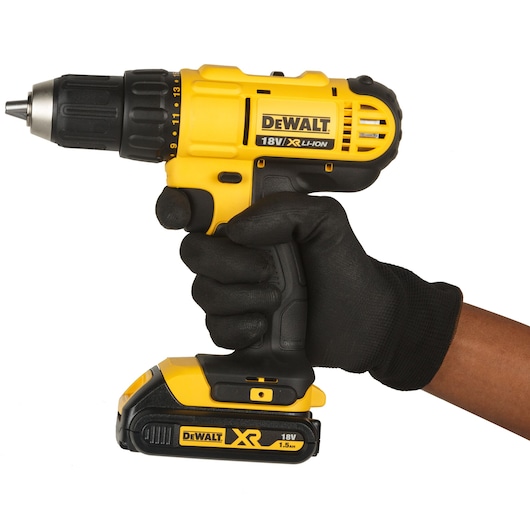 A person wearing a black glove is holding a yellow and black Dewalt 18V cordless power drill.