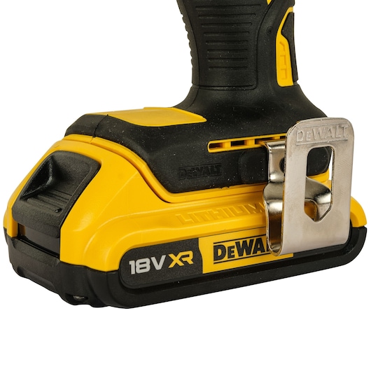 Close-up of the base of a DEWALT cordless power tool showing the 18V XR lithium-ion battery and a metal belt clip attached to the side.