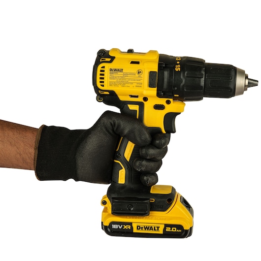 A person wearing a black work glove is holding a yellow and black DEWALT cordless power drill with an 18V XR 2.0Ah battery.