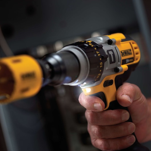 Close-up view of a person holding a DEWALT DCD985M2 cordless drill with a yellow and black design. The drill is in use, and its LED light is illuminated.