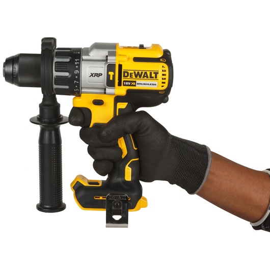 A person wearing a black work glove is holding a yellow and black DEWALT cordless drill with a side handle. The drill is marked with 'XRP', '18V XR', and 'BRUSHLESS'.