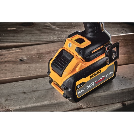 Close-up of a DEWALT XR FlexVolt battery attached to a power tool, showing the 18V/54V and 6Ah specifications. The tool and battery are placed on a wooden surface.