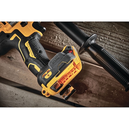 Close-up view of a DEWALT brushless cordless power drill placed on a wooden surface. The drill features a black and yellow body with a textured handle and a detachable side handle.