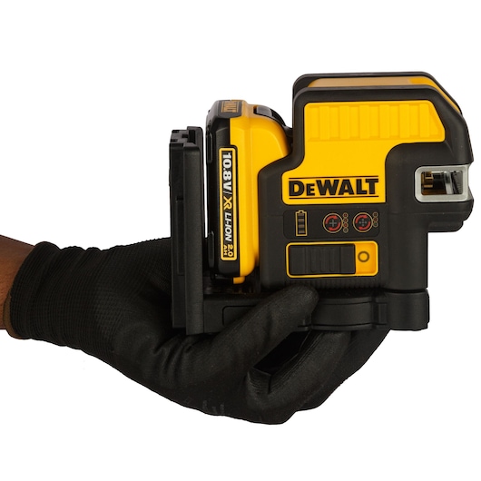 A person wearing a black glove is holding a DEWALT 108V XR Li-Ion 2.0Ah battery-powered device, likely a laser level, used in photography or construction.
