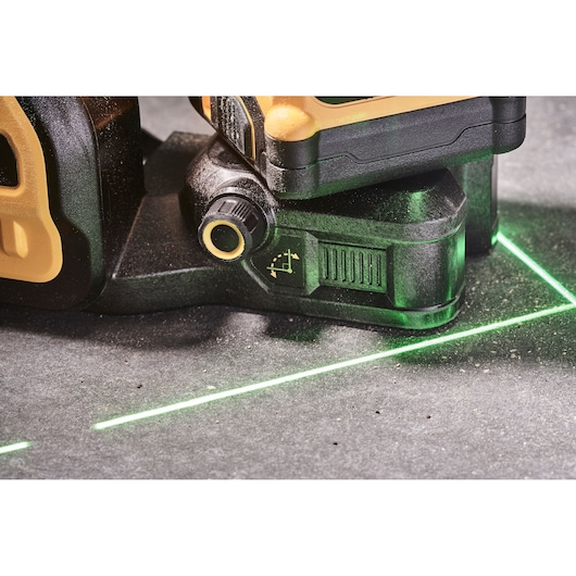 Close-up view of a DEWALT laser level tool projecting green laser lines on a grey surface, used for alignment and leveling tasks.