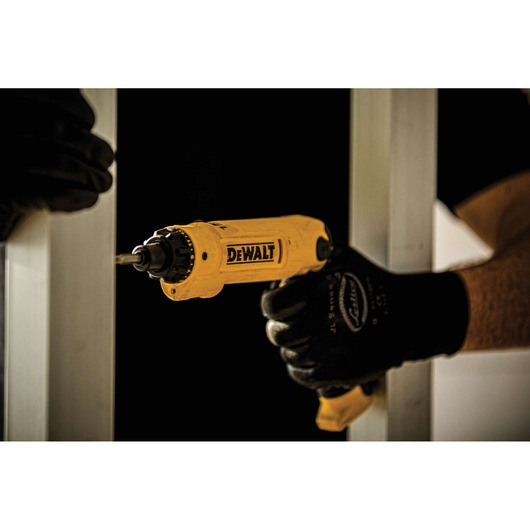 A person wearing black gloves is using a yellow DEWALT electric screwdriver to fasten a screw into a metal frame.