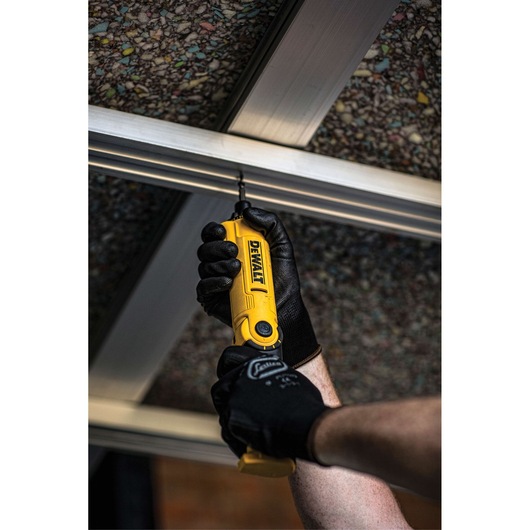 A person wearing black work gloves is using a yellow DEWALT cordless screwdriver to drill into a metal frame on the ceiling.