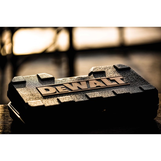 A close-up view of a rugged black DEWALT carrying case, photographed on a table with blurred background and warm lighting.