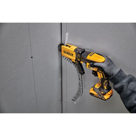 DEWALT drywall screw gun being used with an auto-feed attachment on a gray wall panel.