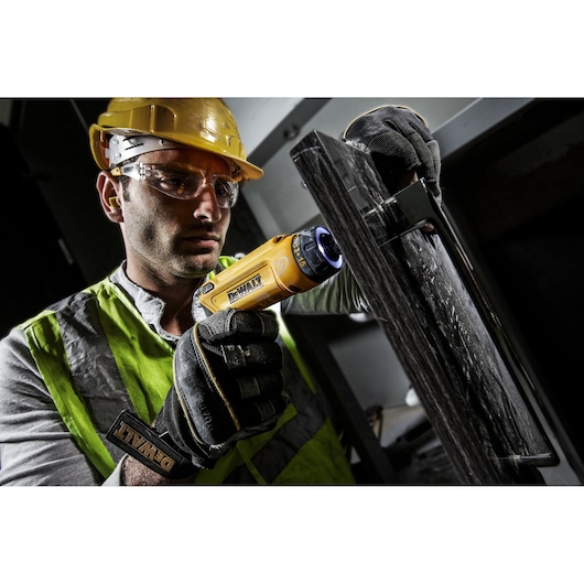 Photo of worker using DEWALT DCF680G2 cordless screwdriver with gloves and safety gear on construction site.