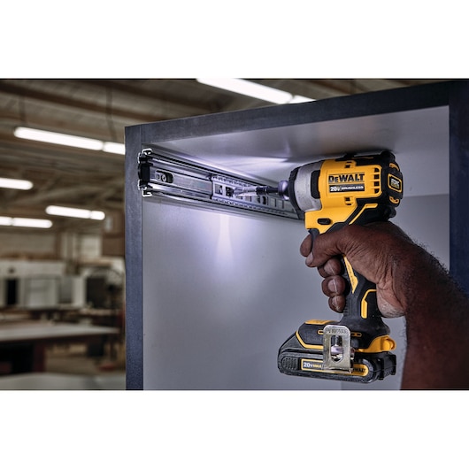 A person using a DEWALT 20V cordless impact driver to install or adjust a metal drawer slide inside a cabinet, in a workshop setting.