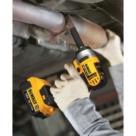 A person wearing gloves uses a DEWALT DCF880M2 cordless impact wrench with an 18V XR Li-Ion battery to work on a metal pipe or automotive part.