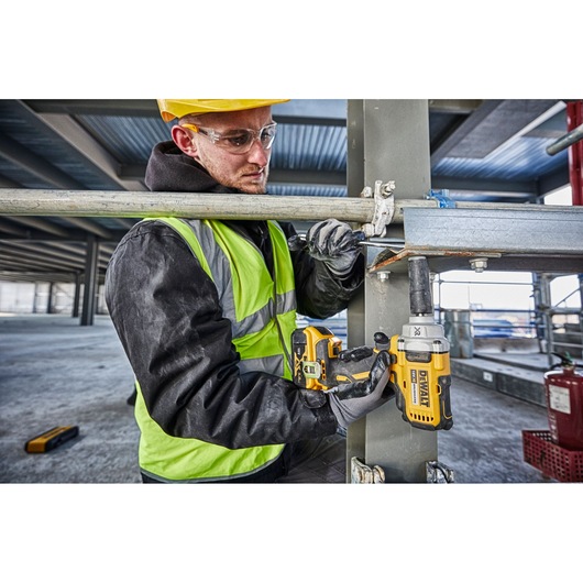 Worker uses a DEWALT DCF894N impact wrench to tighten bolts on a steel structure at a construction site.