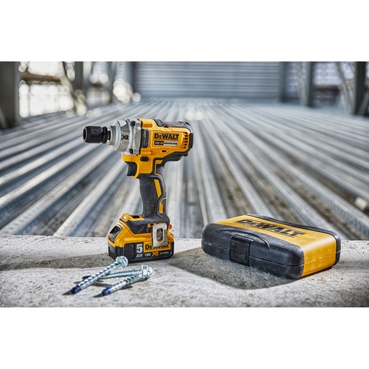 DEWALT cordless impact wrench, sturdy yellow case, and screws on a concrete surface in an industrial setting.