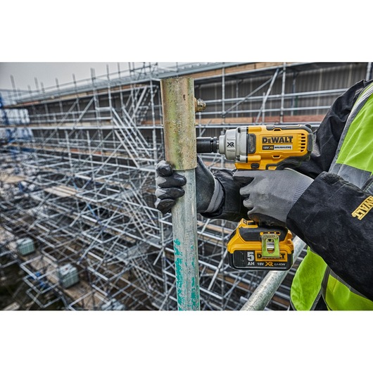 Worker using a DEWALT impact wrench on scaffolding outdoors at a construction site.