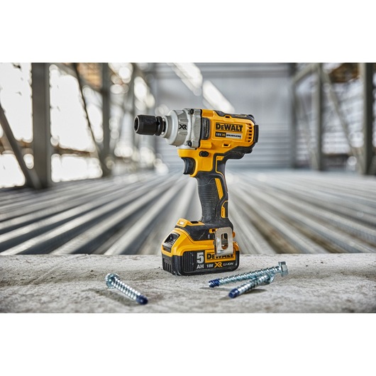 Yellow DEWALT cordless impact wrench on concrete with screws, in an industrial setting.