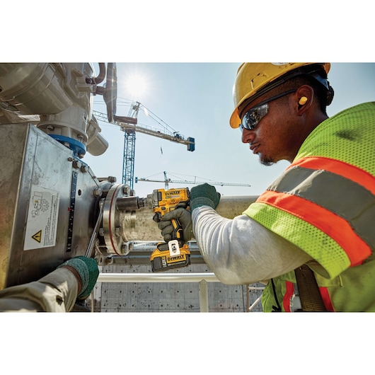 Worker uses a DEWALT DCF894P2 impact wrench on industrial piping at a construction site.
