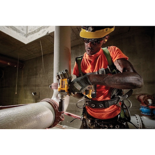 Worker using a DEWALT DCF894P2 power tool on a large pipe at a construction site.