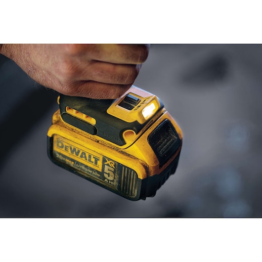Close-up of a hand holding a Dewalt cordless power tool, showing the yellow and black body with a visible battery pack and LED light on top.