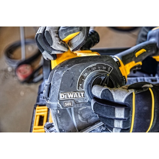 Close-up of a person wearing protective gloves adjusting a setting on a DEWALT 54V power tool.