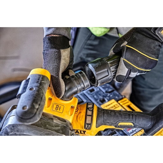 Close-up view of gloved hands connecting a hose to a DEWALT power tool, specifically showing the attachment process and the tool's handle and control buttons.