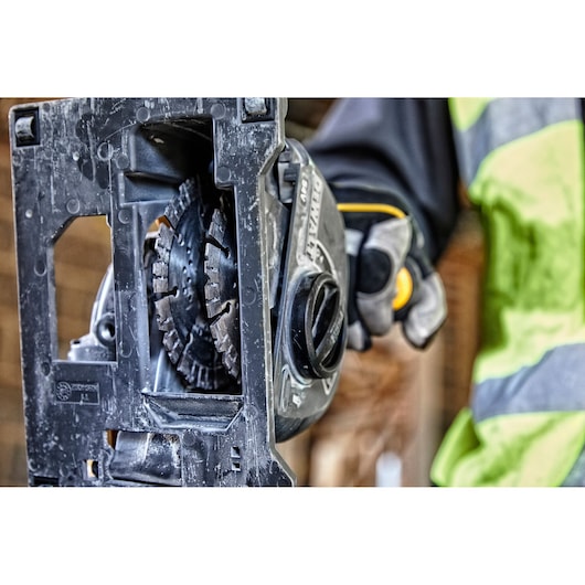 Close-up view of a DEWALT power tool, specifically a cutting or grinding machine, held by a person wearing protective gloves and a high-visibility jacket.