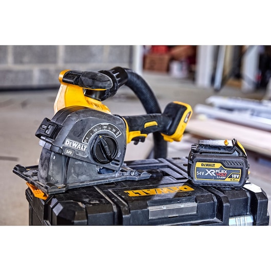 A DEWALT cordless power tool, specifically a wall chaser, is shown with a DEWALT XR FlexVolt lithium-ion battery. Both are placed on a DEWALT storage case, with construction materials visible in the background.