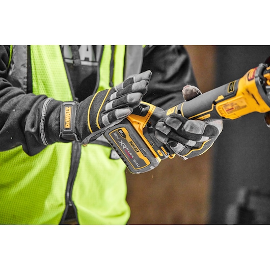Close-up image of a person wearing protective gloves and a high-visibility vest, holding a DEWALT cordless power tool with an XR FLEXVOLT 18V/54V battery attached.