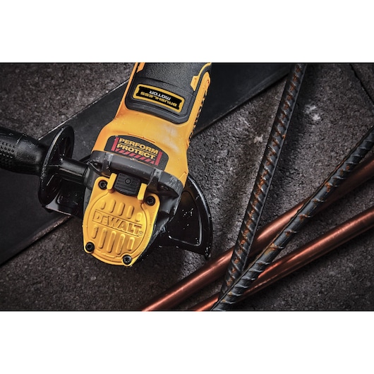 Close-up of a DEWALT cordless angle grinder with a yellow and black design, laying on a rough surface next to metal rods.