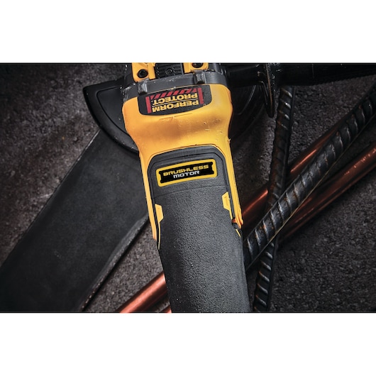 Close-up of a DEWALT power tool handle labeled 'Brushless Motor' and 'Perform Protect', with some metal rods and pipes in the background.